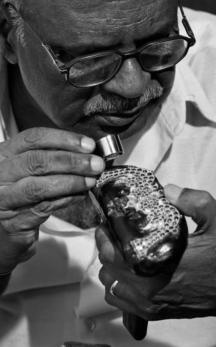Kanak jeweller examining a hand-set piece with a loupe